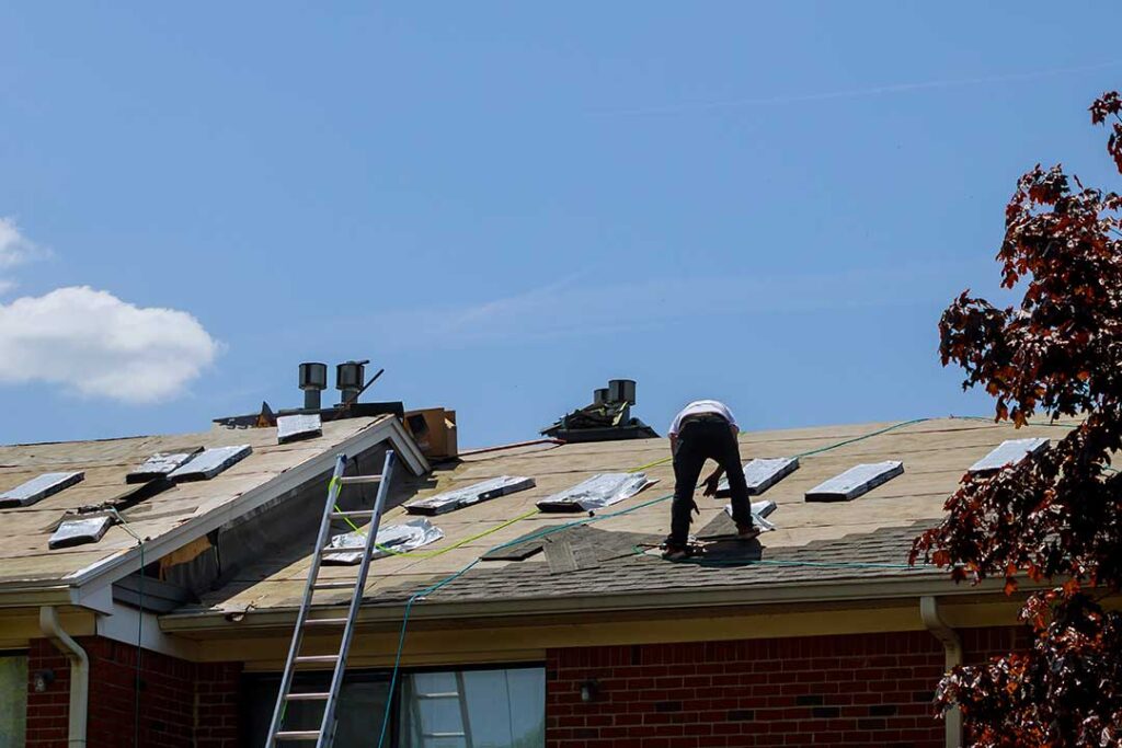 Homeowner comparing roof shingle samples beside a house with siding and exterior trim.