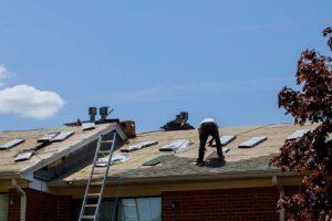 Homeowner comparing roof shingle samples beside a house with siding and exterior trim.