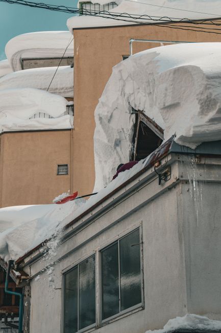 A homeowner observes a snow-covered roof with icicles, gutters, and visible winter wear from the ground.